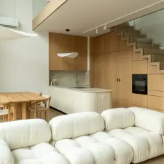 Nowoczesne wnętrze z sofą, stołem i kuchnią. Drewniane schody ze szklaną balustradą.