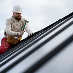 Dekarz w kasku i z młotkiem pracuje na metalowym dachu.