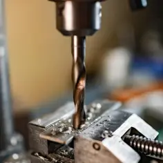 Wiertło wkręca się w metalowy element przytrzymywany przez imadło.